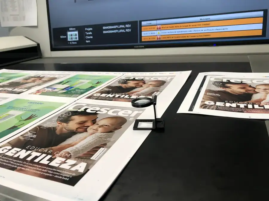 Folhas de capa de revista na mesa de conferência da impressora Komori, com conta-fios